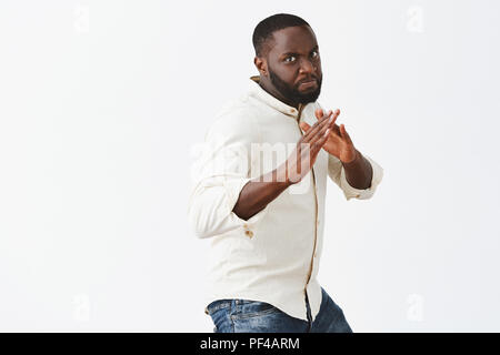 Defend yourself. Portrait of serious-looking strong and funny dark-skinned male model in white casual short standing in martial arts pose, ready to fight raising palms and frowning to scare enemy Stock Photo