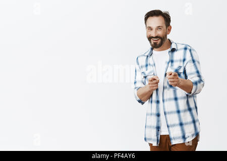 Hey man what is up. Portrait of joyful and friendly happy nice guy with beard and moustache, pointing at camera with index fingers and smiling happily while meeting coworker over grey wall Stock Photo
