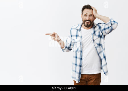 His car broke down, guy asking stranger take him to gas station. Portrait of upset helpless handsome man with beards, pointing left with index finger and holding palm on head, being in tough situation Stock Photo