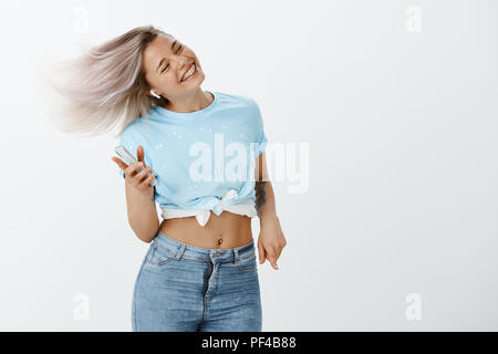 Portrait of positive excited cute woman with braces, jumping and dancing, having fun and enjoying great sound of wireless earphones, listening music and holding smartphone, smiling with closed eyes Stock Photo