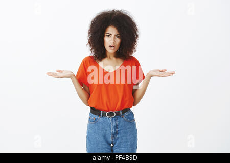 What the hell are you talking about. Portrait of displeased frustrated attractive dark-skinned girlfriend with afro hairstyle, frowning and spreading palms in questioned gesture, being confused Stock Photo