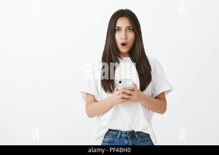 Girl checked mailbox, received fascinating offer. Portrait of stunned emotive young woman with tanned skin, holding smartphone, dropping jaw and saying wow while staring at camera shocked Stock Photo