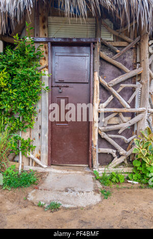 Closed wooden brown grunge door and thatch roof, surrounded by green bushes at Montaza public park, Alexandria, Egypt Stock Photo