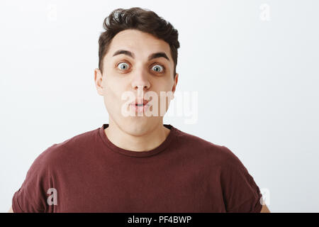 Waist-up shot of funny handsome caucasian guy with short dark hair, saying wow, folding lips and staring with popped eyes at camera while being surprised and amazed with awesome view Stock Photo