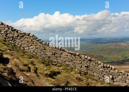 Steep Mourne Wall on Slieve Bearnagh with County Down countryside in background. A granite dry stone wall through the Mourne Mountains, N.Ireland. Stock Photo