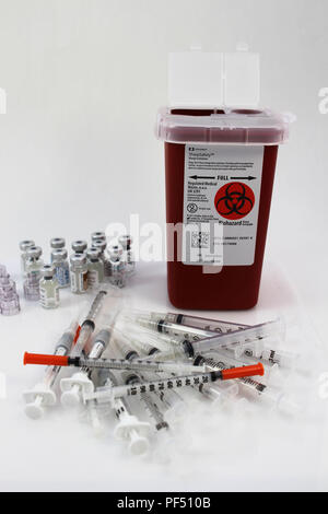 A pile of syringes and vials next to a Sharps container on a white background. IVF treatment / Fertility drugs Stock Photo