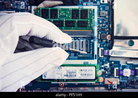 Replacement of memory in the laptop, in one of the service centers for repair of laptops. hand in a white glove holds a screwdriver on the background  Stock Photo