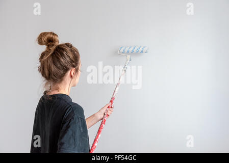 Young woman paints a wall with a roller in a new apartment during a renovation. Stock Photo