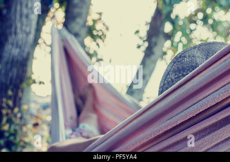 Vintage toned image with an instagram effect of a woman relaxing on a hot summer day in a hammock strung in the shade of a tree. Stock Photo