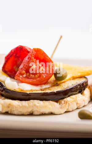 Side view of Italian appetizer of corn cracker topped with baked egg and grilled aubergine and cherry tomatoes. Stock Photo