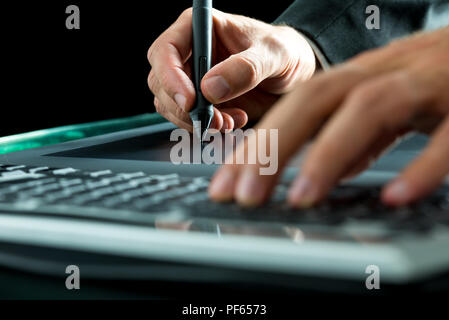 Man using a stylus and tablet while typing on his computer keypad, close up view of his hands. Stock Photo