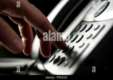 Closeup view of the hand of a man making a telephone call on a desktop instrument pressing the numbers on the keypad Stock Photo
