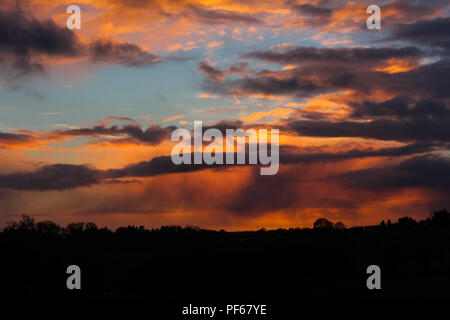 Fiery red sunset skyscape over a silhouetted treeline Stock Photo