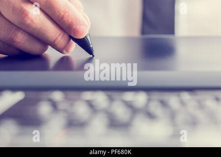 Retro image of male hand of a designer drawing with the stylus on a grey graphics tablet, close-up. Stock Photo