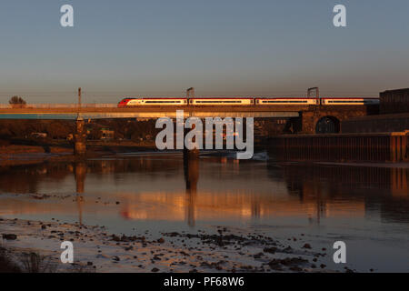 Virgin trains Pendolino 390054 crossing Carlisle Bridge, Lancaster (River Lune) glinting in the sunset and reflected in the river Stock Photo
