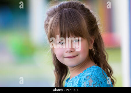 Portrait of little fashionable blond girl in blue dress, with gray eyes and beautiful long hair smiling in camera on bright blurred colorful backgroun Stock Photo