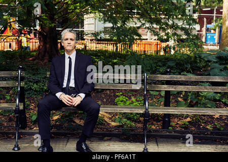 Grey Haired Man in Black Suit Sits on Park Bench Stock Photo