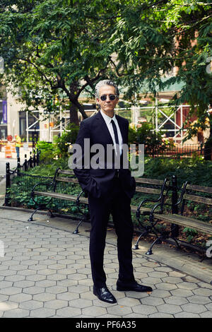 Grey Haired Man in Black Suit Walks Thru a Park Stock Photo