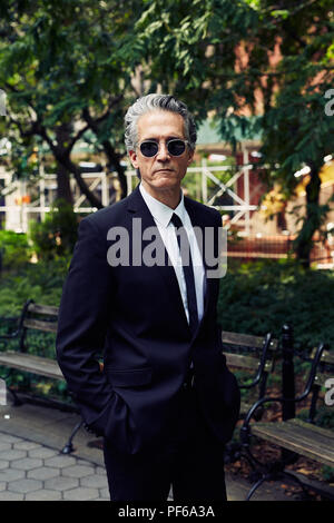 Grey Haired Man in Black Suit Walks Thru a Park Stock Photo