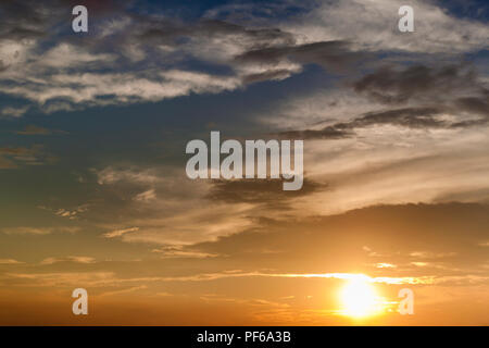 Panorama of sky at sunrise or sunset. Beautiful view of dark, gray and white clouds lit by bright orange yellow sun on clear blue sky. Beauty of natur Stock Photo