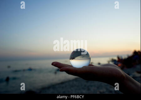 Glass beach on the palm, which reflects the sea, the beach, bathing people.The atmosphere of rest and vacation. Stock Photo
