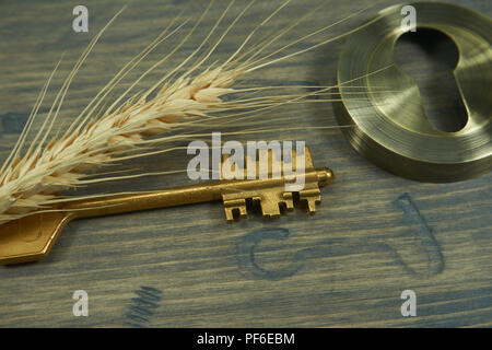 Conceptual close-up of a vintage golden key and ear of wheat on an old wooden table as symbol for access, lucky, property or security. Selective focus Stock Photo
