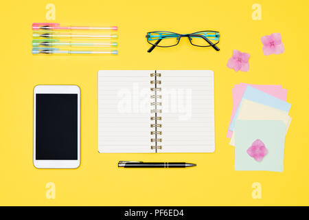 Student desk flat lay. Top view of working space table with open notepad, smartphone and office supplies on pastel yellow colored background. Back to  Stock Photo