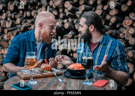 Two bearded men speaking about something while drinking beer Stock Photo