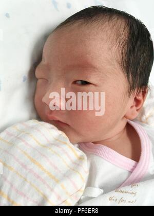 Little cute Asian girl baby lying on the bed is staring with one eye Stock Photo