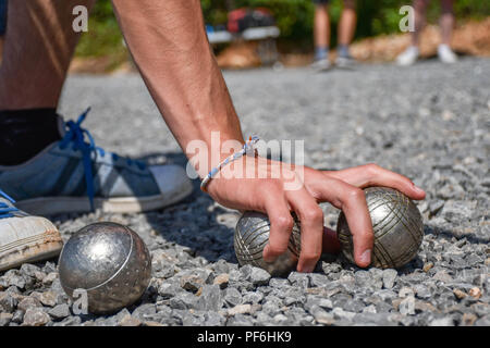 Petanque player grabbing two steel balls on a gravel surface Stock Photo