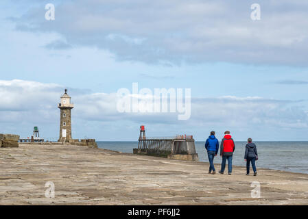 Family walking along the East Pier at Whitby on the coast of North Yorkshire, England. A mature couple and son stroll towards the lighthouse. Stock Photo