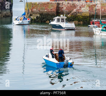Dunbar, East Lothian, Scotland, United Kingdom, 20th August 2018. UK Sunshine in Dunbar harbour. Two men leave the harbour in a small boat with moored boats including a fishing boat and yachts