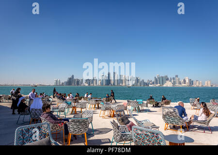 Doha, Qatar - Jan 8th 2018 - Locals and tourists enjoying a cafe bar with Doha's skyline in the background in a blue sky day, Doha in Qatar Stock Photo
