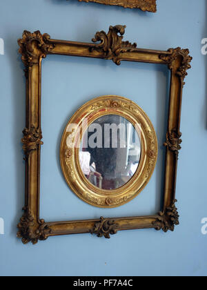 Two Gold picture frames with no pictures in the frames hanging on walls with plain background. Centre oval frame has a mirror. Property released Stock Photo