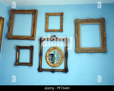 Large collection of Gilt Gold picture frames with no pictures in the frames  hanging on walls with plain background. Property released Stock Photo