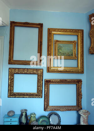 Large collection of Gilt Gold picture frames with no pictures in the frames  hanging on walls with plain background. Property released Stock Photo