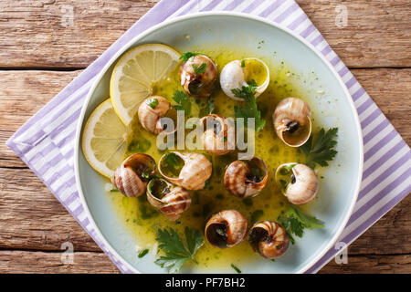 Edible snails, escalgot with butter, herbs and garlic close-up on a plate on a table. Vertical top view from above Stock Photo