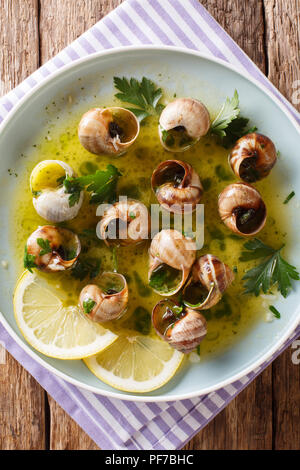 Spicy French snails, escargot cooked with butter, parsley, lemon and garlic close-up on a plate on a table. Vertical top view from above Stock Photo