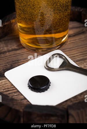 Beer coaster with bottle top and opener and glass of beer on top of wood barrel. Stock Photo