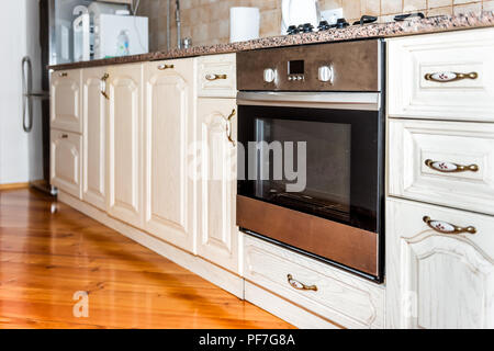 Modern wooden brown kitchen features cabinets with granite countertops and tile backsplash with closeup of dirty oven Stock Photo