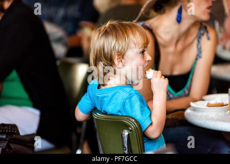 New Orleans, USA - April 22, 2018: Famous Cafe Du Monde cafe restaurant in Louisian old town city with young boy child eating popular pastry beignets 