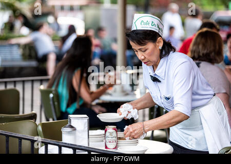 New Orleans, USA - April 23, 2018: Female waitress, woman cleaning up with people sitting at table at famous, iconic Cafe Du Monde shop, serving beign Stock Photo