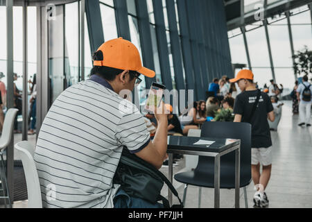 London, UK - June 24, 2018: Young man sitting in a cafe inside Sky Garden, London, playing a game on his mobile phone. Sky Garden is the highest publi Stock Photo