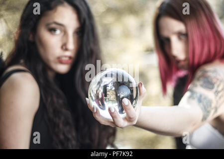 Two girls dressed in black and white are predicting the future with a crystal ball at the pier of a forest. Stock Photo