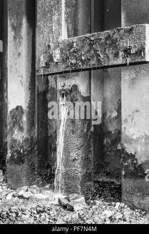 Black and white image of metal reinforcement pilings on the south bank of the River Thames, water gushing from drainage outlets, Bankside, London, UK Stock Photo