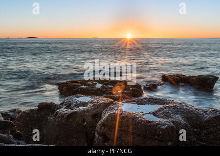 Star burst sunrise over a rocky beach Stock Photo