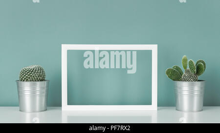 Collection of various cactus plants in metal pots. Potted cactus plants on white shelf against turquoise colored wall and picture frame mock up. Stock Photo