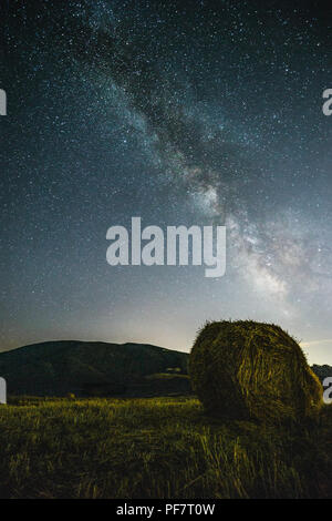 Beautiful view of starred night sky with milky way over a cultivated field with hay bale Stock Photo