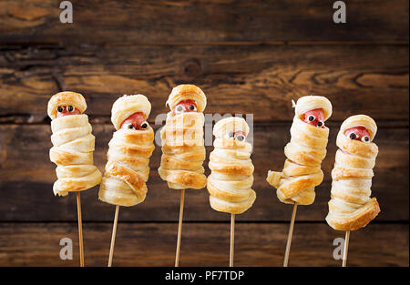 Scary sausage mummies in dough with funny eyes on table.  Halloween food. Top view. Flat lay Stock Photo