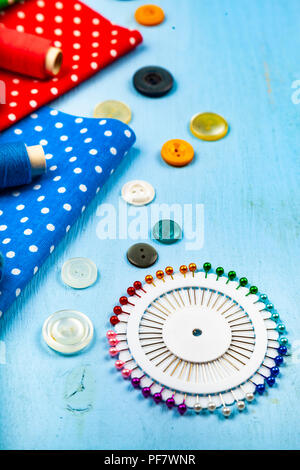 Sewing accessories and multi-colored fabrics on a blue wooden background. Fabrics, measuring tape, pins, buttons and thread. Stock Photo
